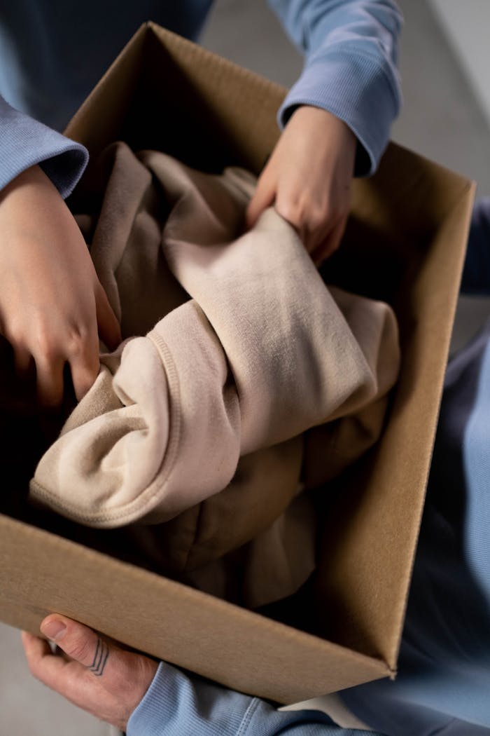 Close-up of hands sorting clothes into a cardboard box for charity donations.