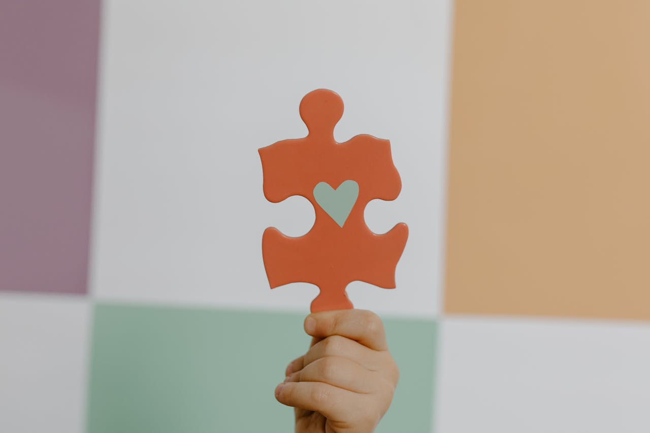 A hand holds a red puzzle piece with a heart, symbolizing connection and awareness.